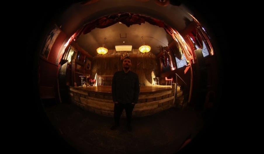 Event poster for a performance by Nick Tudor & Gee Sonnet, featuring a fisheye photo of a person standing in a warmly lit venue. The event is on Thurs