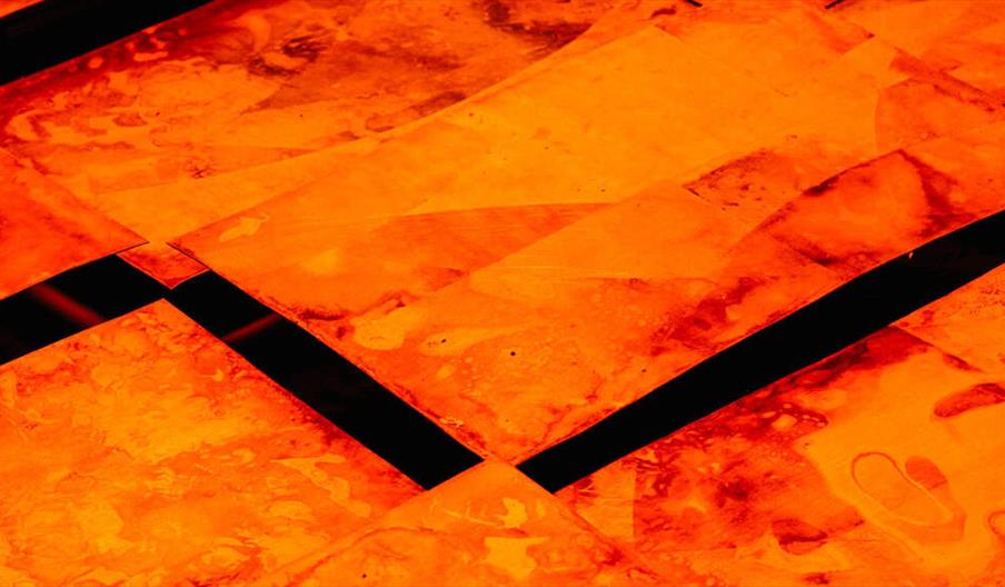 Abstract close-up image of orange-red, marbled translucent sheets arranged in a grid with dark, straight gaps intersecting between them.