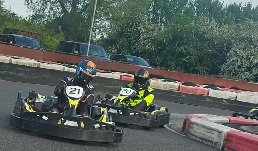 Two racers in go-karts drive around a course.