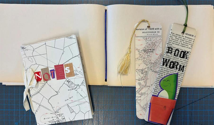 A notebook with a cover featuring a map design and the word "NOTES" in colorful, cut-out letters is placed on top of an open, blank sketchbook. Next t