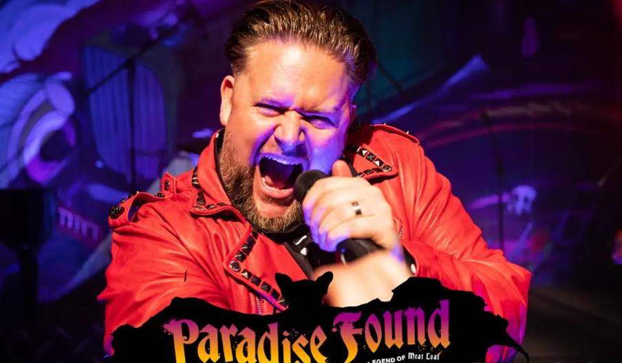 A man wearing a bright red jacket passionately sings into a microphone on stage, illuminated by colorful stage lights, with the words "Paradise Found"