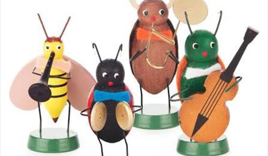 Five whimsical insect figurines made of painted materials are arranged like a musical band, each holding a different instrument including a trumpet, d