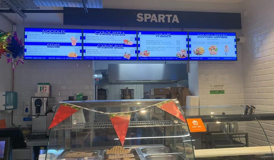 The counter of Sparta Kitchen, with a salad bar and signs showing the different gyros available.