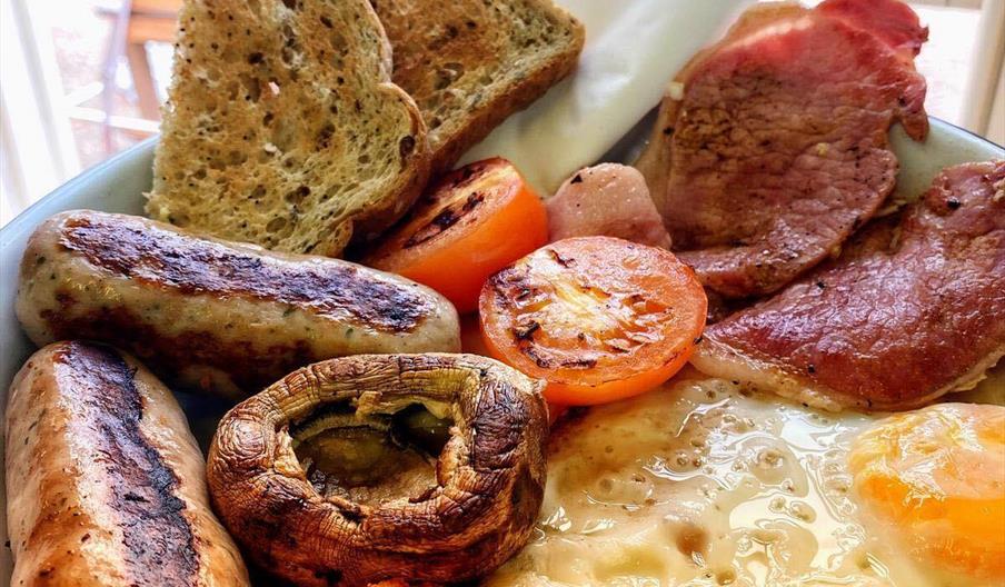 A plate filled with staples of a full english breakfast, such as hash browns, eggs, bacon, tomatoes, sausages, wholemeal toast and mushrooms.