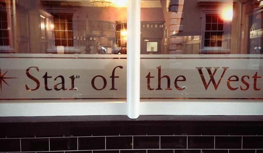 The window of Star of the West with black brickwork below. The name of the Pub is depicted in frosted glass.