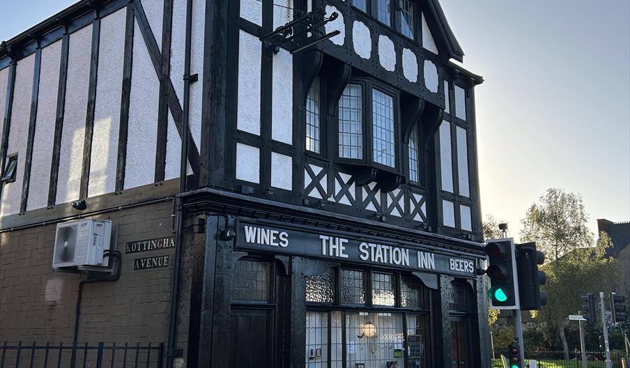 The exterior of The Station Inn, an old building with white walls and black timber and ornate windows.
