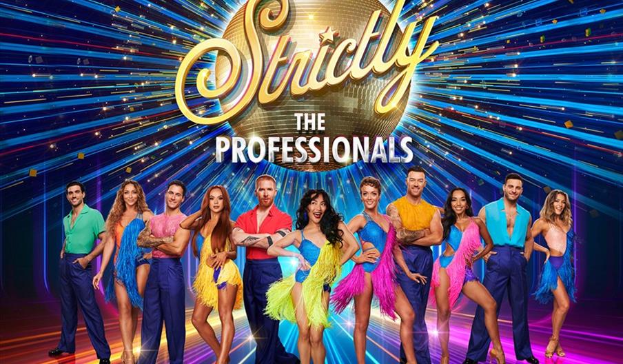 A group of eleven professional dancers pose in colorful costumes in front of a sparkling gold disco ball with the words "Strictly The Professionals,"