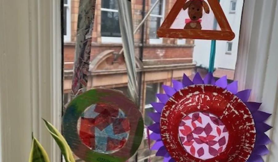 Colourful paper crafts, including a triangular shape with a dog drawing, a red and green circular decoration, and a red and purple flower-like paper p