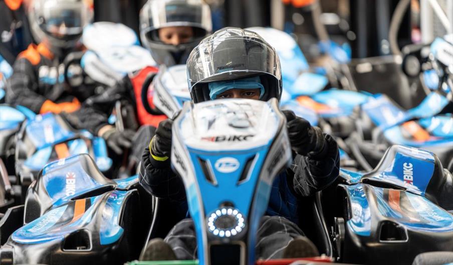 Several blue go-karts lined up ready to drive with their drivers.