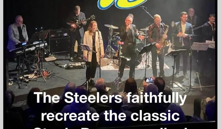 A band performs on stage in front of an audience with text above and below the photo reading, "The Steelers playing the music of Steely Dan" and "The