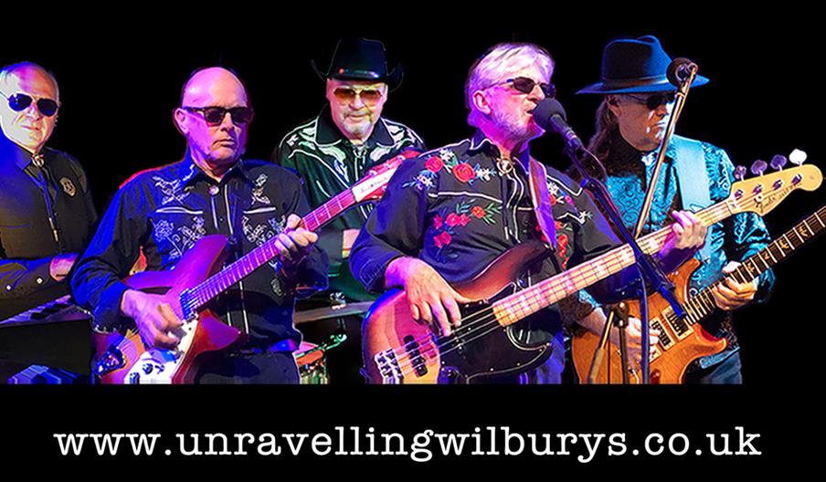 Five male musicians in matching embroidered shirts perform with guitars and a keyboard against a black background, with the website "www.unravellingwi