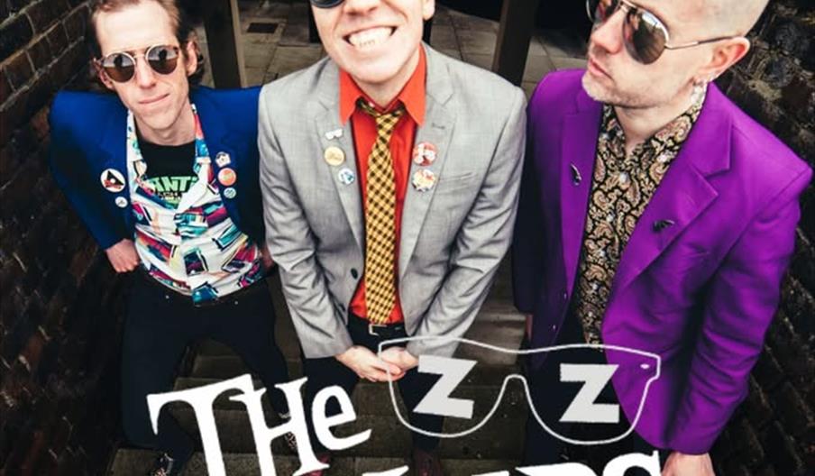 Poster for a music event featuring the band The Zipheads, showing three band members in colorful suits and sunglasses standing on stairs, with event d