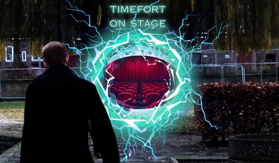 A person in a dark coat stands outdoors, facing a glowing, electric portal displaying a theater with red seats and a red curtain inside; above the por