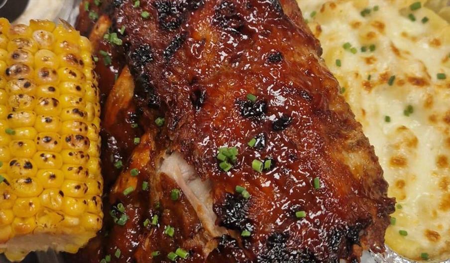 Corn on the Cob, ribs and mac and cheese with chives in a metal tray.