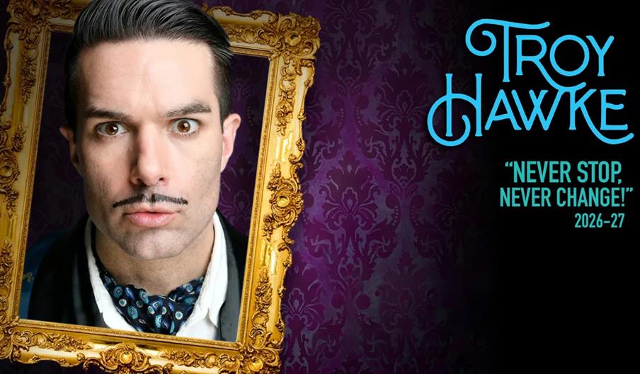 A man with slicked dark hair, a thin mustache, and a cravat gazes intensely out of a gilded picture frame against a purple patterned wallpaper backgro