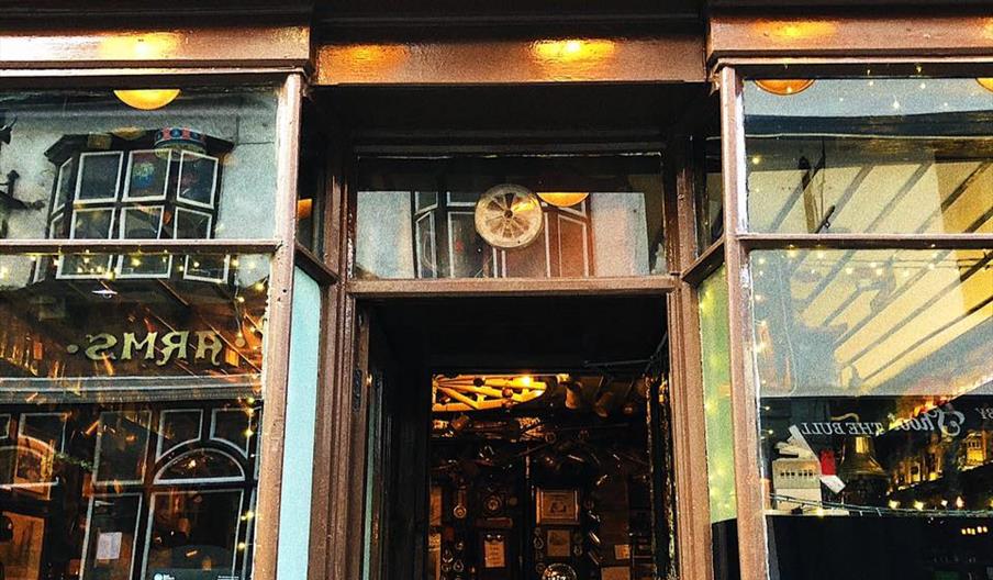 The street view of Wm Hawkes, a brown building with fairylights in the windows, curved lights lining the roof edge and a gold cursive logo reading 'Wm