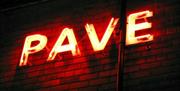 Bright red neon sign on a brick wall spelling the word "PAVE."