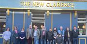 Group of people standing outside The New Clarence pub, Hull, with a blue and gold frontage and the pub name displayed above them