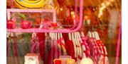 A shop window display with a pink shelf holding whimsical items including a large banana, glass cherries, a vase, cute food-themed mugs and toast with
