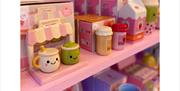 A display shelf filled with colourful, ceramic kitchen items shaped like cute drinks and food with smiling faces, including mugs, shakers, and novelty