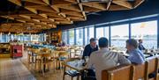 nside of restaurant, large windows with view of the River Hull, wooden tables and chairs and several groups of people eating and chatting