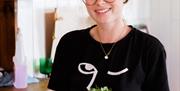 Interior of Thieving Harry's. A smiling woman wearing glasses and a black shirt holds a bowl of salad with various toppings, standing indoors near a r
