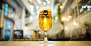 A glass of beer with the BrewDog Logo on, sat on a wooden tabletop with a bar in the background.