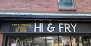 Exterior of a brick building with a sign reading "HI & FRY" above the entrance. To the left, a board displays "Cafe & Takeaway" with opening hours, an