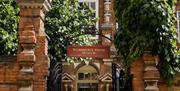 The front gates to the Wilberforce House Museum, with red brick walls either side and foilage spilling over the sides. A hallway leads further into th