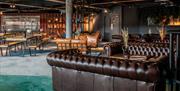 Leather sofas and modern style picnic benches inside BrewDog with a window hatch to the kitchen behind.