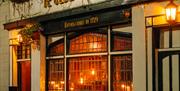 Nighttime street view of "Ye Olde Black Boy" pub with illuminated signage, hanging plants, and vintage-style windows and doors.