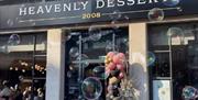Exterior of "Heavenly Desserts" decorated with a pastel balloon arrangement and a dried floral display. The building features tall windows and columns