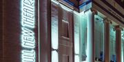 Nighttime view of Hull New Theatre’s exterior, featuring tall illuminated white columns and a vertical neon sign reading "Hull New Theatre" on a brick