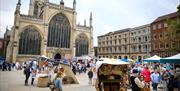 A daytime image of Hull Minster, a large gothic style Minster with stained glass windows and spires. In front there are several gazebos and medieval s