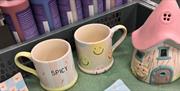Hand-painted ceramic mugs and a small pottery house at Cozy Kiln studio in Hull.