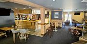 Bar area with three steps leading down, wooden stools, tables chairs and a wall mounted TV.