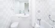Hotel bathroom with tub, sink and toilet all white and fully tiled