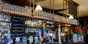 Interior of The Minerva. A traditional pub bar with dark wood paneling, multiple beer taps, shelves of spirits and glassware, and a sign above promoti