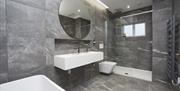 Fully tiled bathroom with large round mirror and walkin shower.