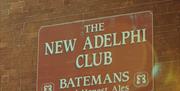 A red sign on a brick wall reads "The New Adelphi Club. Batemans Good Honest Ales" with decorative logos in the corners.