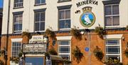 A vintage-style gin van is parked in front of The Minerva pub, a two-story brick building with flower boxes under the windows and a painted crest on t