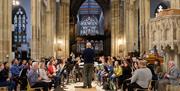 Inside Hull Minster a woodwind orchestra is seated in the middle of the space, witha conductor standing in front of them on a small platform. Large st