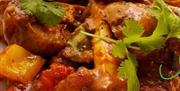 Close-up of a plate of chicken curry with chunks of chicken, potatoes, and bell peppers in a rich, reddish-brown sauce, garnished with fresh cilantro