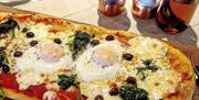 Large pizza with spinach and egg on wooden board along with salt, pepper and oilve oil dispenser