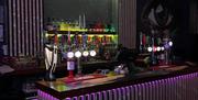Interior of Monroes Bar. A modern bar with illuminated "MONROE'S" sign above shelves of various liquor bottles, multiple beer taps on the counter, and