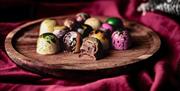Collection of colouful chocolates on a circular, wooden board surrounded by a purple, velvet cloth.