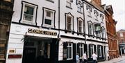 A white, historic-looking building with a sign reading "George Hotel" above an entrance; four people are walking on the cobblestone street in front of