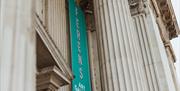 A tall turquoise banner reading "Ferens Art Gallery" hangs between large ornate stone columns on the facade of a grand neoclassical building.