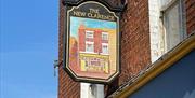 A hanging sign on a brick building reads "The New Clarence" and features a painted image of a red-brick pub façade under a blue sky.
