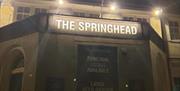 A nighttime photo of a building with an illuminated sign reading "THE SPRINGHEAD" above the entrance. Below, a board advertises function rooms availab